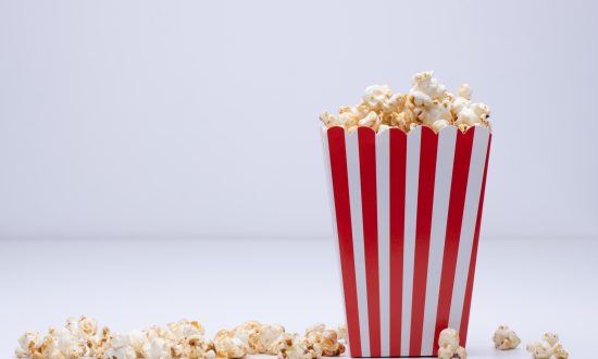 Paper cup of popcorn and some popcorn scattered around on a white surface